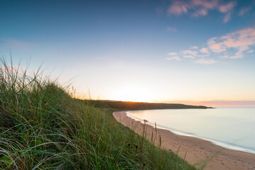 Melvich Bay. Scotland, NC500 route. Golden sunset over calm beach with dunes and grass at the horizon