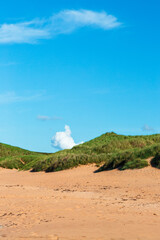 Melvich Bay. Scotland, NC500 route. Sunny beach dunes with green grass, clear blue sky, and white clouds