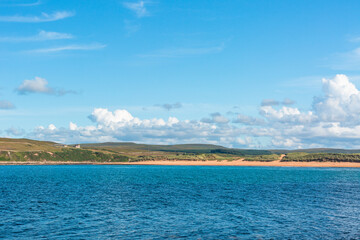Melvich Bay. Scotland, NC500 route. Calm coastal seascape with blue water, sandy beach, and open sky under bright clouds above