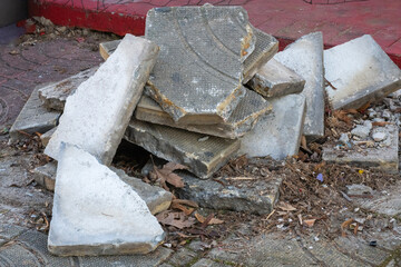a messy pile of broken grey concrete paving slabs and debris stacked on a paved surface near a red curb.