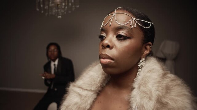 Close up shot of fashionable African American woman with evening makeup posing in studio while wearing fur coat and rhinestone head chain with matching earrings, slow motion