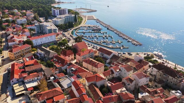 Aerial drone view of a coastal neighborhood with red roofed houses, narrow streets, and a small marina along the shoreline. Biograd na Moru, Croatia