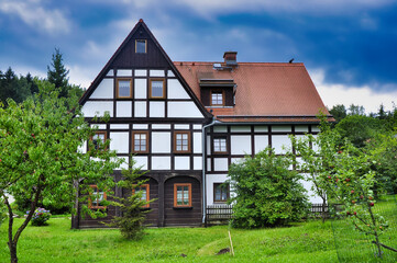 Tradycyjny dom z muru pruskiego z czerwonymi dachami, białymi ścianami i bujnym ogrodem. Historyczny górski kurort Kurort Jonsdorf. © Pol Badger