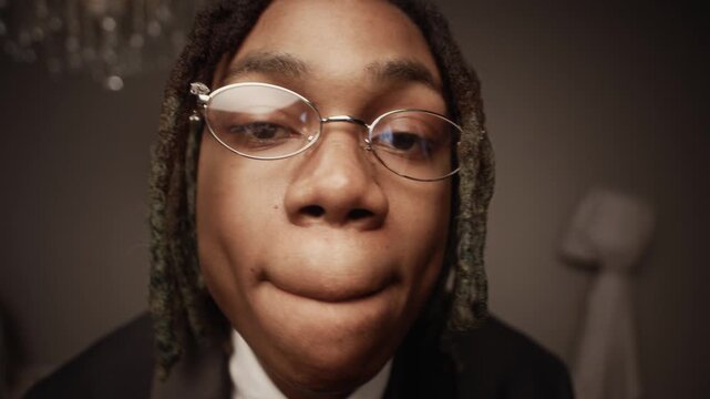 Close up shot of young African American male rapper wearing silver grillz and trendy eyeglasses gesturing toward camera while recording dynamic music video in studio