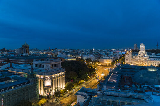 Aerial view of the illuminated Metropolis Building and the Cibeles Palace shining majestically against the deep blue twilight sky, Madrid, Community of Madrid, Spain.