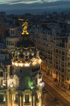 Aerial view of the illuminated Metropolis Building's golden statue against the fading twilight sky, standing tall amidst the urban tapestry, Madrid, Community of Madrid, Spain.
