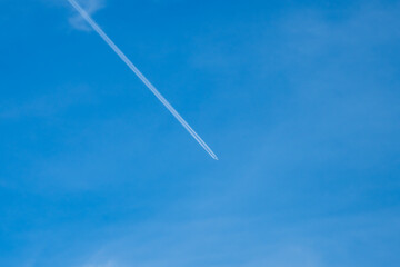 A minimalist view of a clear blue sky with a distinct white airplane contrail stretching diagonally across the frame.