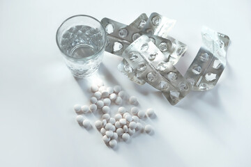 glass with water, pile of tablets, used blisters on light background close up. organic supplement for health care. medical drugs overdose concept. top view. copy space