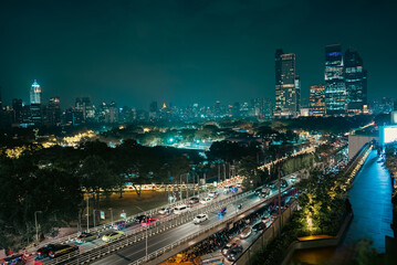 Obraz premium illuminated big city skyline at night, cars on road at rush hour, Lumpini park with festive street lights, high-rise skyscrapers and downtown glow at evening, Dusit Central, Bangkok Thailand