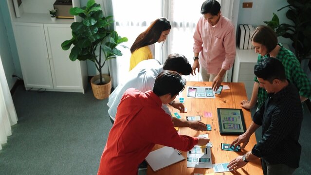 Top view of caucasian developer group planning for digital wireframe design. Skilled diverse designer in casual outfits brainstorming or working together to design mobile app interface. Convocation. - Powered by Adobe