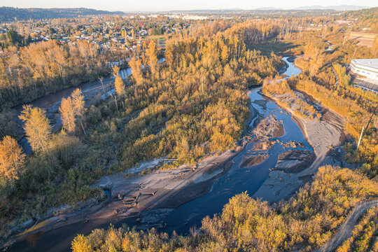 Aerial view of the winding river cutting through the landscape, bordered by trees displaying their autumnal colors, creating a vibrant contrast against the water, Auburn, Washington, United States.