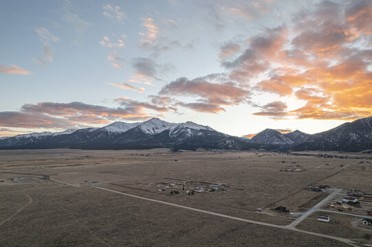 Aerial view of the vast, tawny plains stretching to meet the snow-dusted peaks under a sky ablaze with hues of apricot and lavender at sunset, Buena Vista, Colorado, United States.