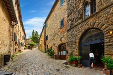 Fototapeta premium A young female server waits in a doorway on a picturesque cobblestone alley in the medieval hill town of Volterra, Italy, Tuscany region.