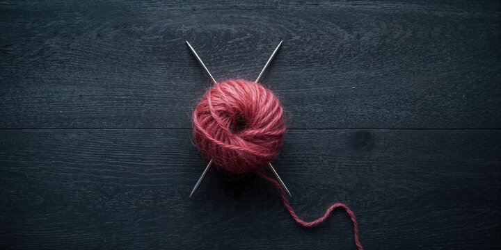 Knitting tools and wool ball arranged on a dark gray wooden table, ideal for textile layout backgrounds