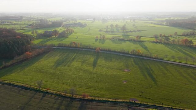Aerial view of rural fields with crop rows, tree shadows, canal, and farm buildings sunlit landscape blending agriculture, infrastructure, and natural geometry.