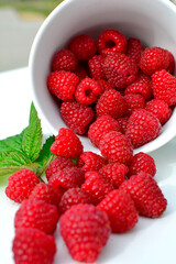 maliny w białym kubku, czerwone maliny, maliny z zielonym liściem, fresh raspberries in a cup, red raspberries, juicy raspberries with a green leaf, Rubus idaeus, rasberry view from above, białe tło © kateej