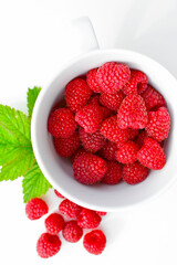 maliny w białym kubku, czerwone maliny, maliny z zielonym liściem, fresh raspberries in a cup, red raspberries, juicy raspberries with a green leaf, Rubus idaeus, rasberry view from above, białe tło © kateej