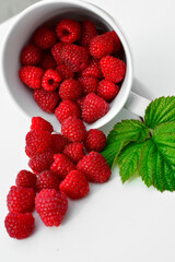 maliny w białym kubku, czerwone maliny, maliny z zielonym liściem, fresh raspberries in a cup, red raspberries, juicy raspberries with a green leaf, Rubus idaeus, rasberry view from above, białe tło © kateej
