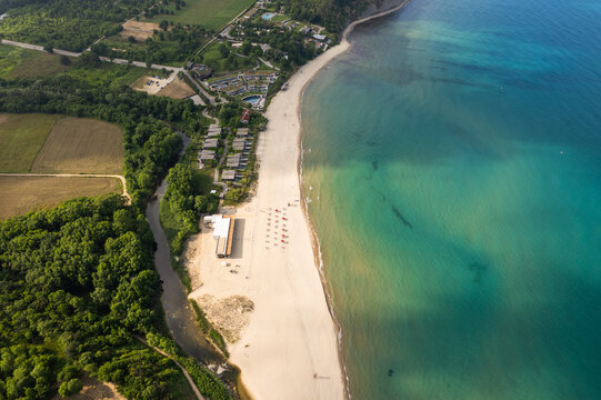 Aerial view of the shoreline where azure waters meet the sandy beach, bordered by green trees and buildings, Vaya Beach, Burgas, Bulgaria.