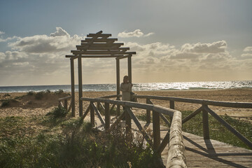 Woman contemplating ocean view from wooden boardwalk pergola