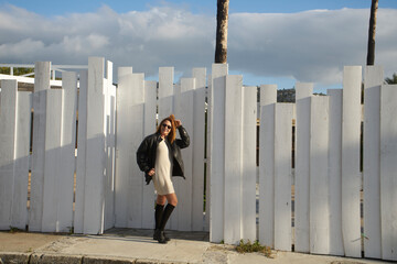 Woman posing in street style fashion by white fence