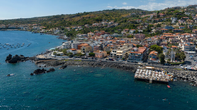 Aerial view of the Aci Trezza waterfront overlooking the Mediterranean Sea, in the province of Catania, Sicily, Italy. In the background is the center of the town. It's a sunny summer morning.