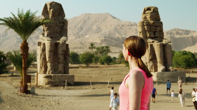 A female tourist looks at the Colossi of Memnon, a giant statue in Luxor, Egypt. An ancient historical landmark of Egypt during the time of the pharaohs.