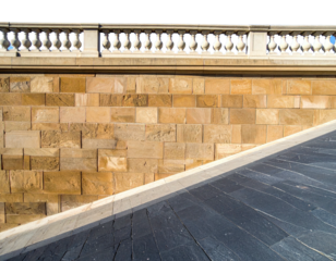 Stone wall with a balustrade above, and a dark paved walkway in the foreground