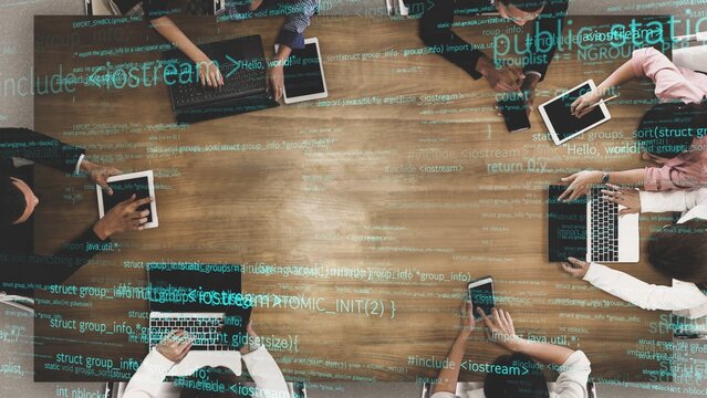 A diverse group of professionals collaborates in a modern workspace, using laptops and tablets to engage in coding and technology projects, showcasing teamwork and innovation. Xenic - Powered by Adobe