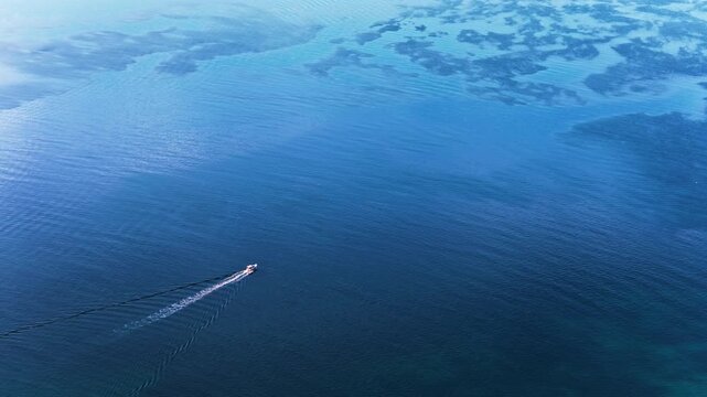 Aerial drone view of open blue water with a small motorboat moving across the frame, leaving a long wake behind