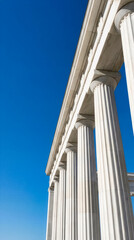 White classical columns of neoclassical government building facade against blue sky. Stone architecture with fluted pillars and capitals on historic structure.
