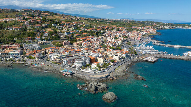 Aerial view of the town of Aci Trezza overlooking the Mediterranean Sea, in the province of Catania, Sicily, Italy. In the background is the marina of the city. It's a sunny summer morning.