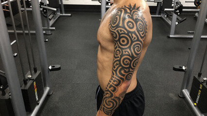 Full sleeve spiral tribal tattoo on sweaty muscular arm in fitness center