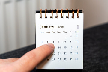 A hand points at January 6 on a calendar for 2026, showcasing the start of the month. The scene...