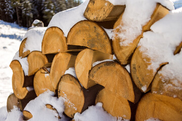 Neatly piled stack of chopped dry trunks wood covered with snow outdoors on bright cold winter sunny day, abstract background, Fire wood logs prepared for winter, ready for burning.