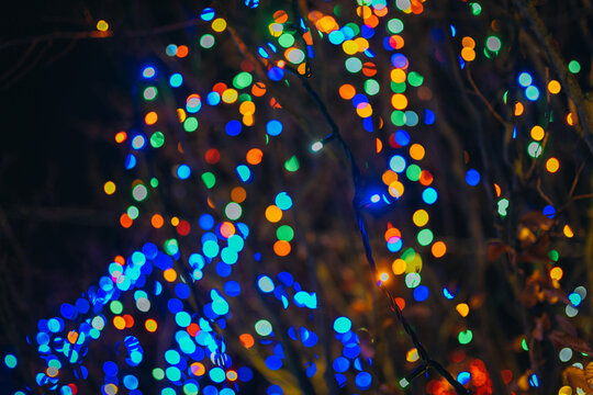 An abstract festive background of bright, multicolored Christmas lights in out-of-focus bokeh. Blue, yellow, green, and red glowing spots against a dark background. - Powered by Adobe