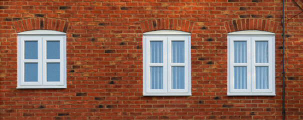Three white multi pane windows with brick arches on a red brick building facade, creating a repetitive architectural pattern