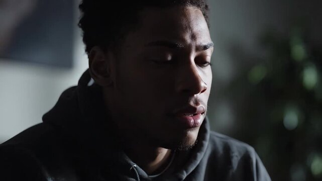 Close-up of a sad young Black man looking down in guilt. Depressed male feeling anxious and worried in dim lighting. Mental health concept