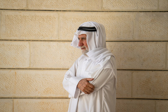 An adult Muslim man in white traditional clothes looks at the camera and expresses emotions. Elderly male sheikh on a background. High quality photo