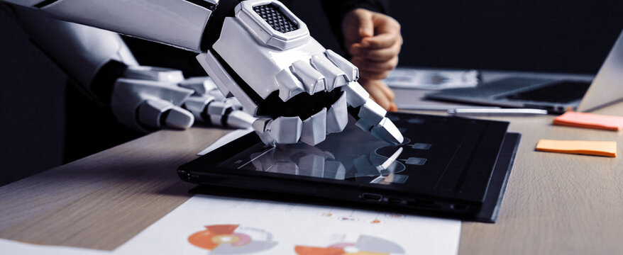 A robotic hand engages with a touchscreen laptop in a modern workspace. A human presence suggests collaboration on data analysis, showcasing innovation.Noogenesis - Powered by Adobe