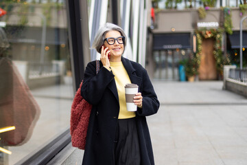Fototapeta premium Senior woman smiling, talking on phone, walking urban street