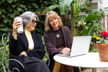 Senior women friends using laptop outdoors
