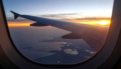 Obraz premium 夕焼けに染まる空を背景に飛行機の窓から旅客機の翼と景色を眺める情緒的な時間