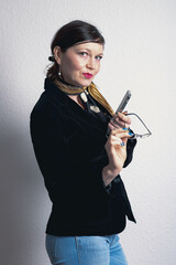 A woman in a black jacket and glasses is holding a cell phone and a pair of glasses. She has a serious expression on her face