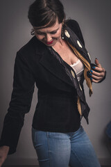 A woman in a black jacket and blue jeans is wearing a black tie and a white bra. She is smiling and she is happy