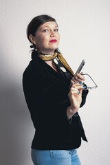 A woman in a black jacket and glasses is holding a cell phone. She is wearing a yellow scarf and has blue nail polish