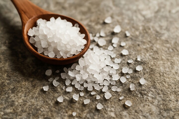 Coarse White Sea Salt Crystals in Wooden Spoon on Textured Stone Background