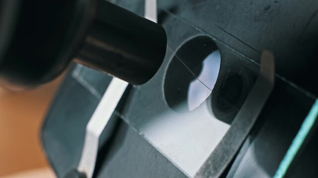 Close-up of a pipette dripping clear liquid onto a glass slide on a microscope stage. The metal objective lens is visible during sample preparation for analysis.