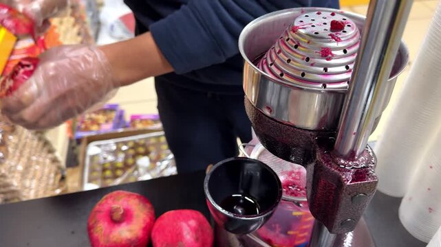 Street food vendor squeezing fresh ripe pomegranates with a manual press to make a healthy, organic red juice for a customer in an outdoor market, showcasing a small business in action