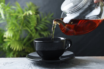 Woman pouring hot tea into cup from teapot at grey table, closeup. Space for text
